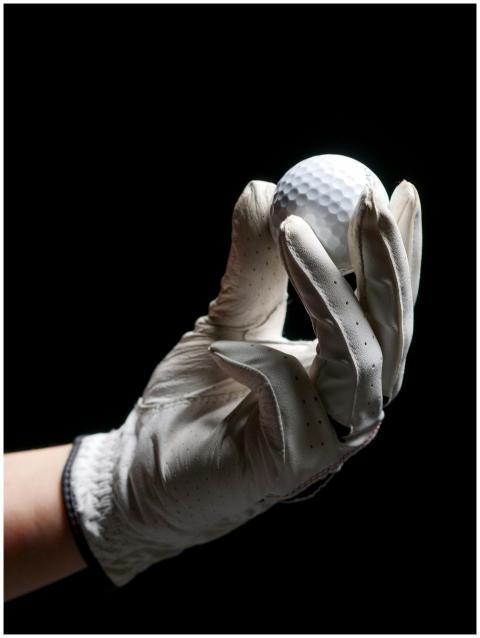 A gloved hand elegantly holds a golf ball against