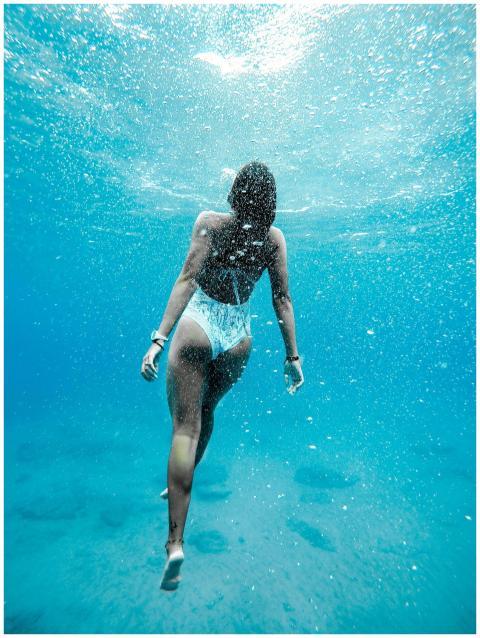 Woman swimming underwater with bubbles in blue oce