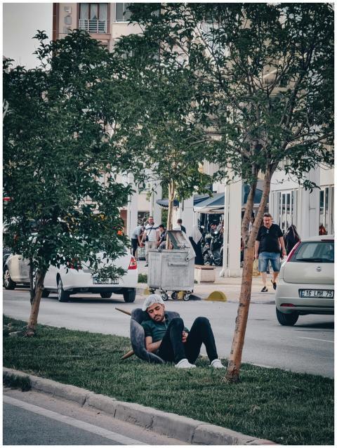 A man wearing a cap rests on the grass by a busy u