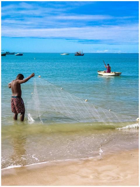 A fisherman casting a net on a sunny beach in Bahi