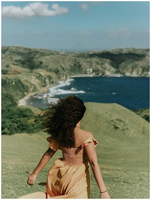 A woman stands on a grassy hill overlooking the st