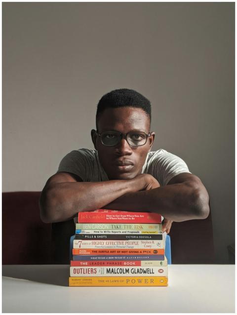 A man with eyeglasses sitting indoors, leaning on