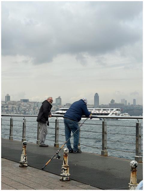 Two men fishing from a pier in İstanbul with city