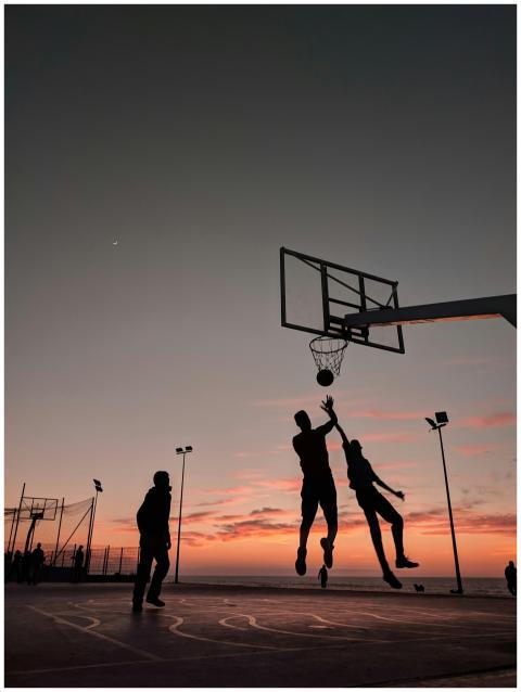 Silhouetted players jump for a basketball during a