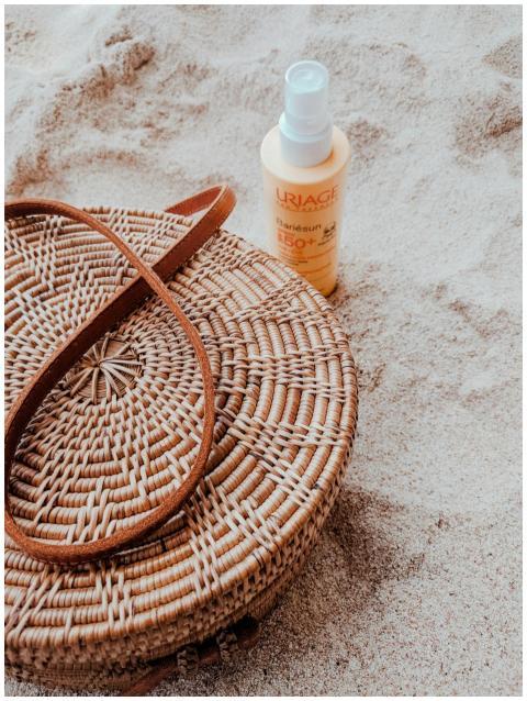 A wicker bag and sunscreen lotion set on the sandy