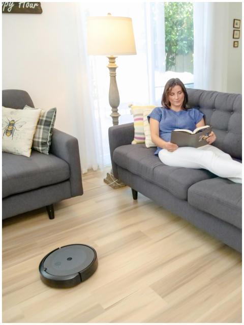 Woman reads on a sofa while a robotic vacuum clean