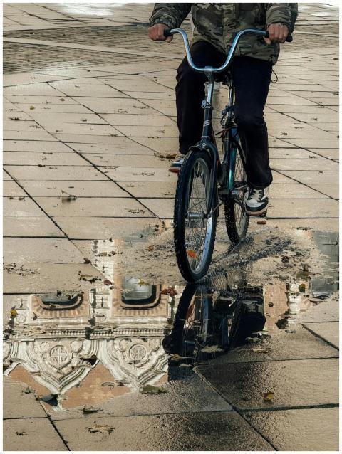 A cyclist passes a puddle reflecting a historic bu
