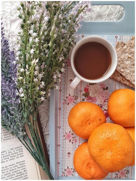 Flat lay of coffee, oranges, flowers, and a book f