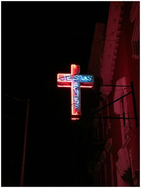 A glowing neon cross sign that reads 'Jesus Saves'
