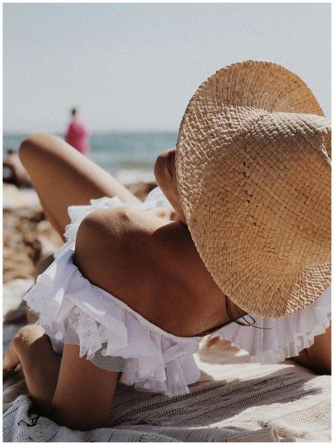 Woman lounging on a beach in a straw hat and off-s