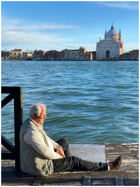 An elderly man sits by the canal in Venice, enjoyi