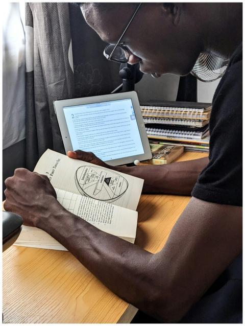 A man studying with a book and tablet at a desk in