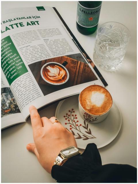 Hand holding a latte art magazine open beside a ca