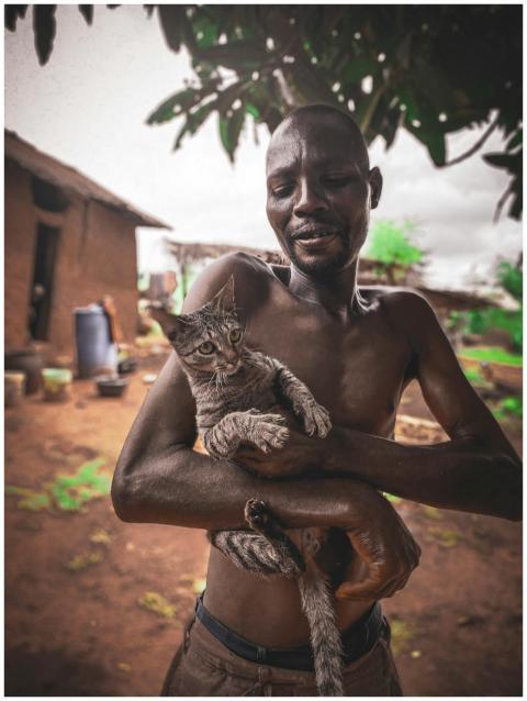A man gently holding a tabby cat in a rural area o