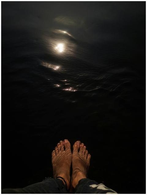 Feet by water reflecting the moonlight at night, c