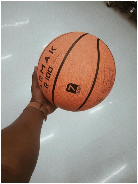 A hand gripping an orange basketball indoors showi