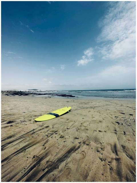 A lone yellow surfboard rests on a tranquil beach