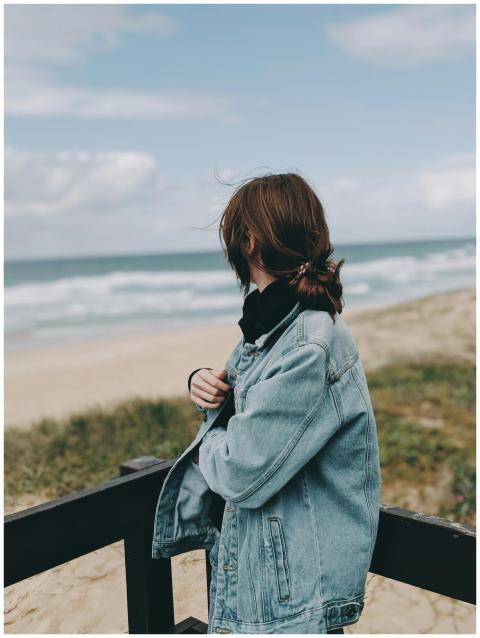 A woman stands by a beach, gazing at the ocean in