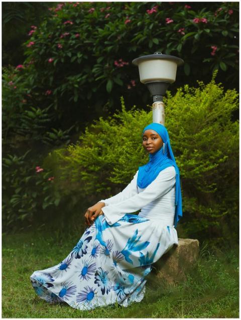 Young woman in blue hijab and floral dress sitting