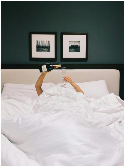 A person celebrates with champagne in bed, capturi