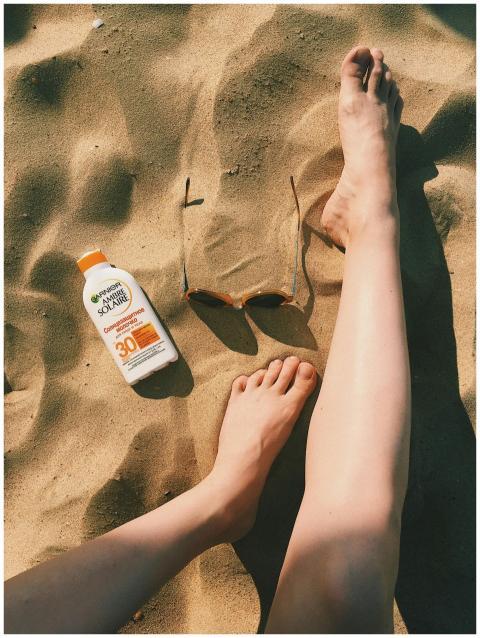 Feet on sandy beach with sunscreen bottle and sung