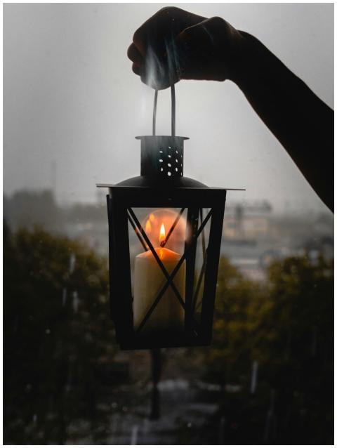 A glowing candle lantern held up against a rainy n
