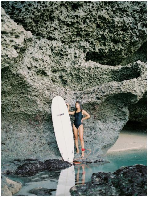 Woman in black swimsuit standing with surfboard by