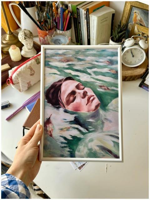 A hand holds a portrait painting in an artist's st