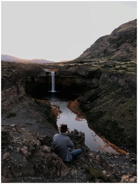 A lone traveler by a waterfall, surrounded by a dr