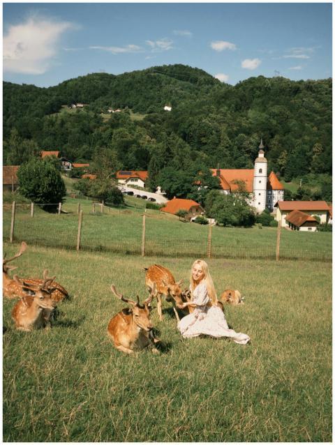 A woman sits among deer in a picturesque Slovenian