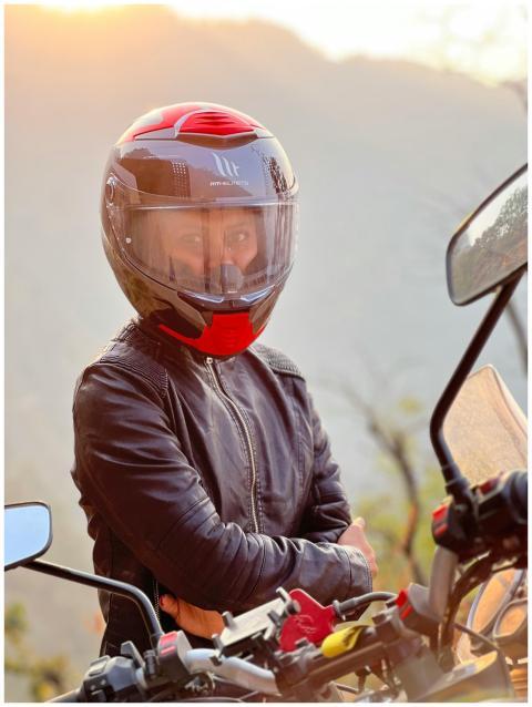 A motorcyclist wearing a helmet and jacket stands