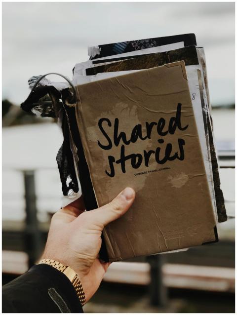 Hand holds a "Shared Stories" journal against a bl