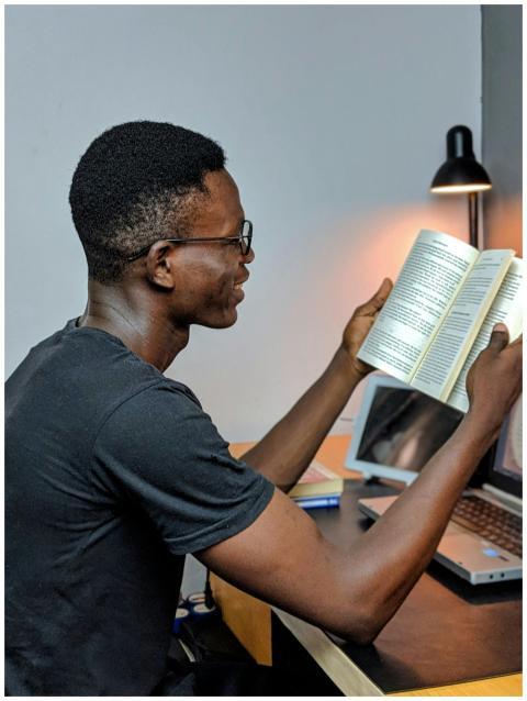 African man engaged in reading at a study desk, il