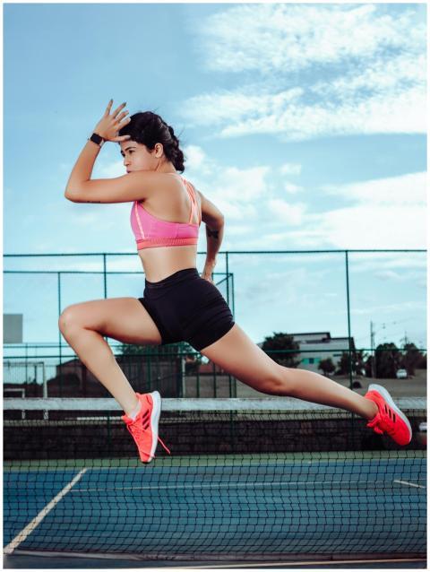 Athletic woman jumping energetically on a tennis c