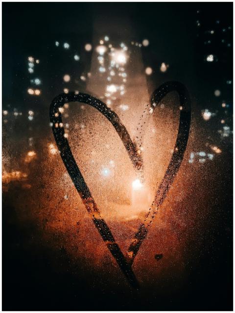 Heart drawn on glass of wet window with view of li