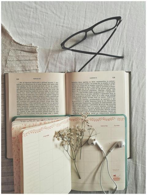 Flat lay of an open book, planner, and eyeglasses