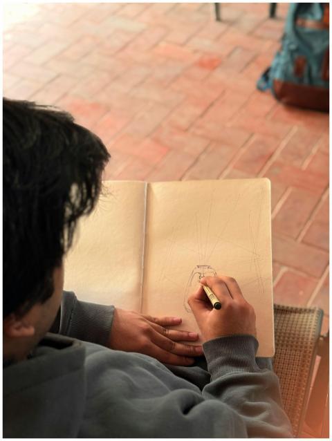 A person sketching in a notebook on a brick patio