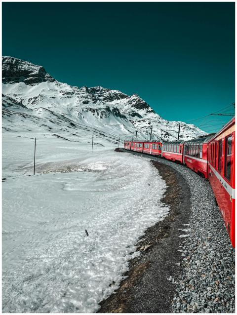 A red train travels through snow-covered mountains