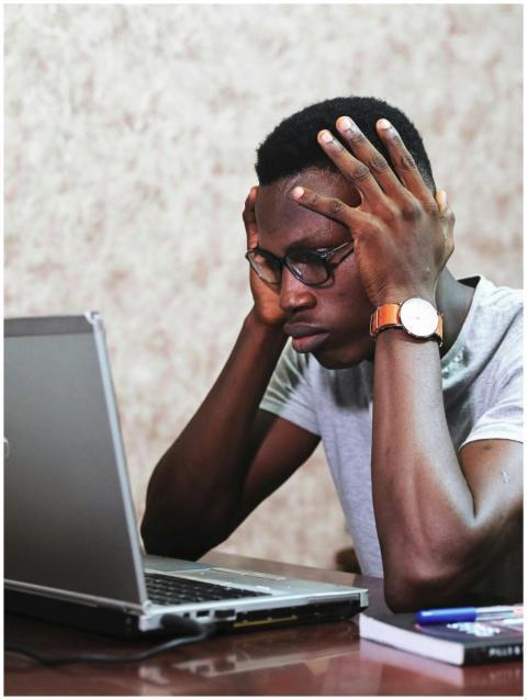 A man appears frustrated while working on a laptop