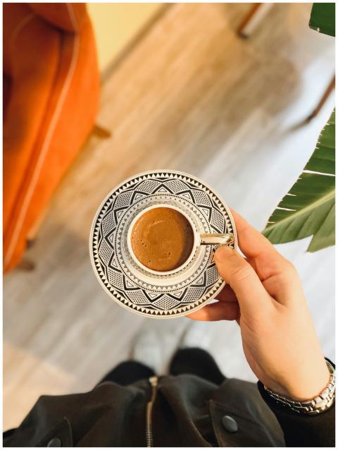 Hand holding a decorative coffee cup over a stylis