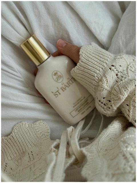 A hand in a sweater holds a luxury body lotion bot