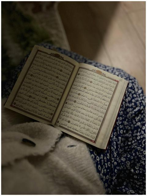 An open Quran on a lap with a blue floral backgrou