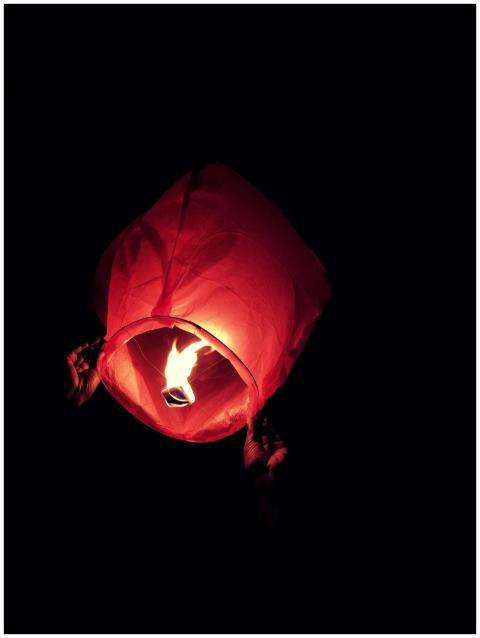 Close-up of hands releasing a sky lantern, illumin