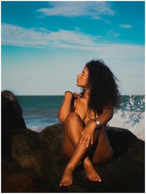 A beautiful woman in a bikini poses on ocean rocks