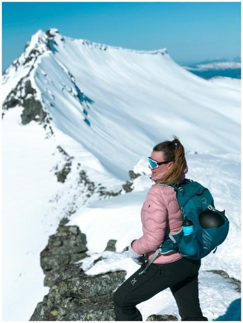 A woman in winter gear hiking atop a snowy mountai