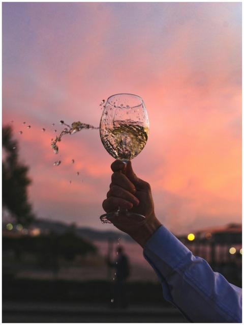 A hand holding a splashing glass of white wine aga