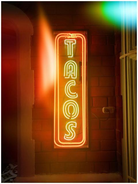 Bright neon tacos sign illuminated on a rustic bri