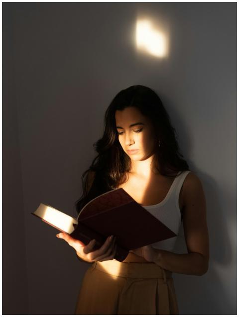 A woman stands reading a book in soft natural ligh