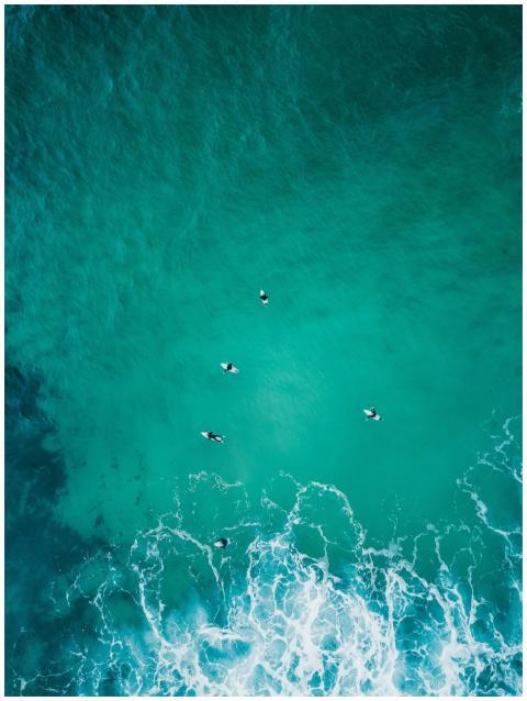 Aerial view of surfers riding turquoise waves at M