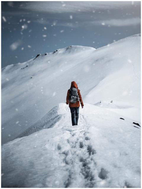 A lone hiker in a red jacket walks up a snow-cover